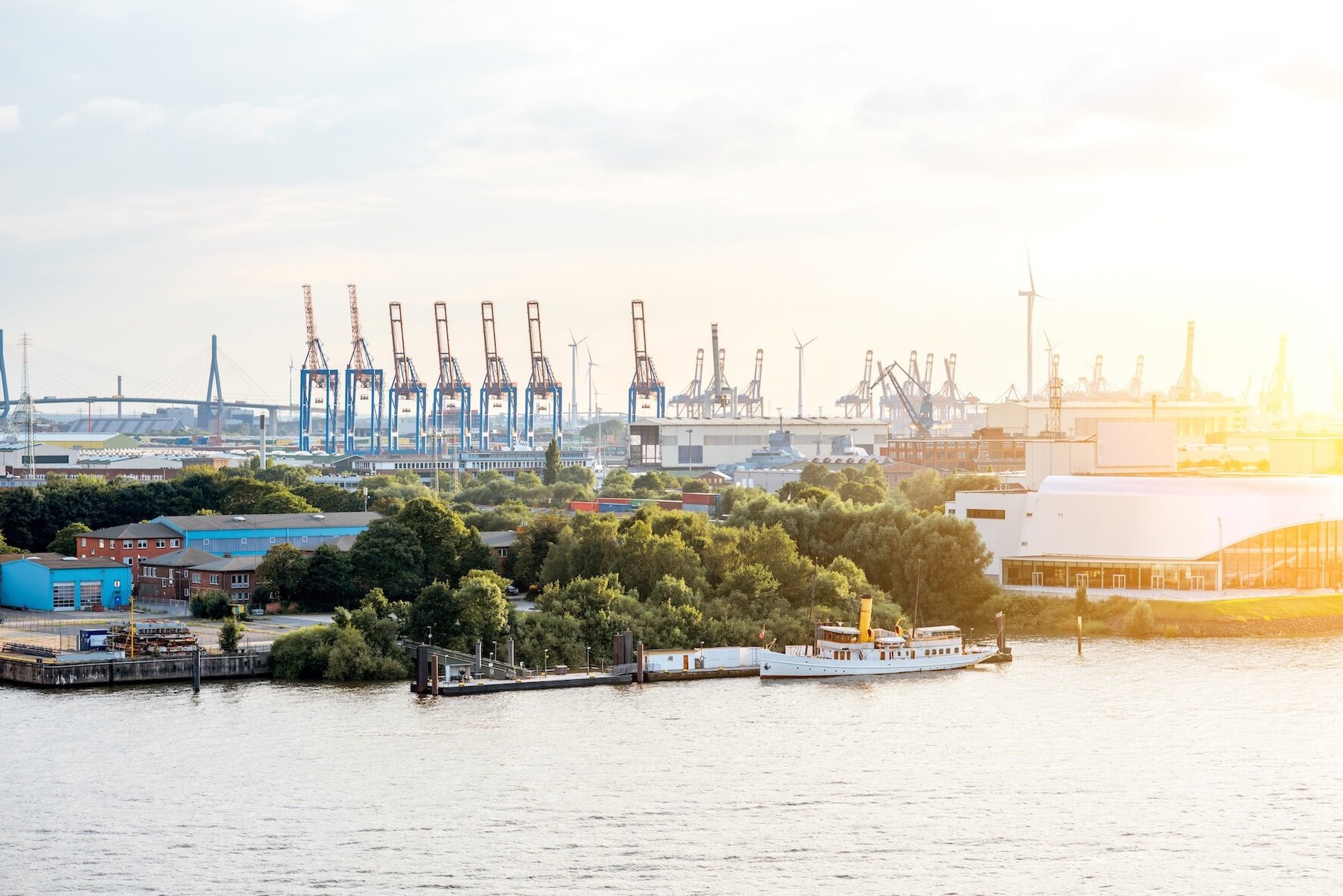 Port cranes in Hamburg, wind turbines, and a ship at sunset